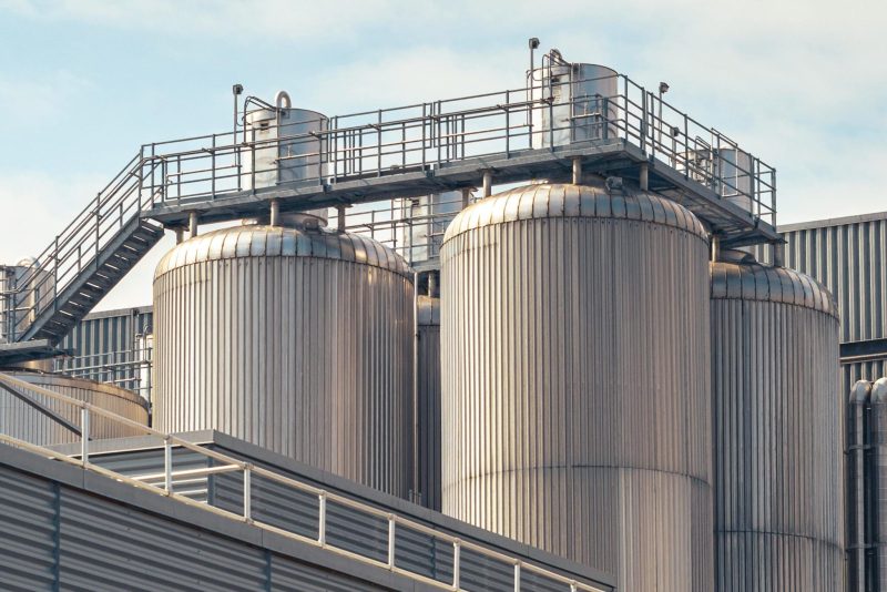 A view of metal storage tanks outside an industrial facility under a partly cloudy sky.